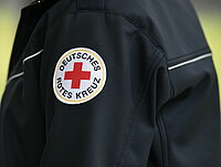 Das Foto zeigt einen DRK Helfer in blauer Einsatzjacke mit DRK Logo