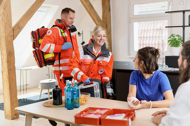 Das Foto zeigt zwei Notfallsanitäter bei einer Patientin im Wohnzimmer